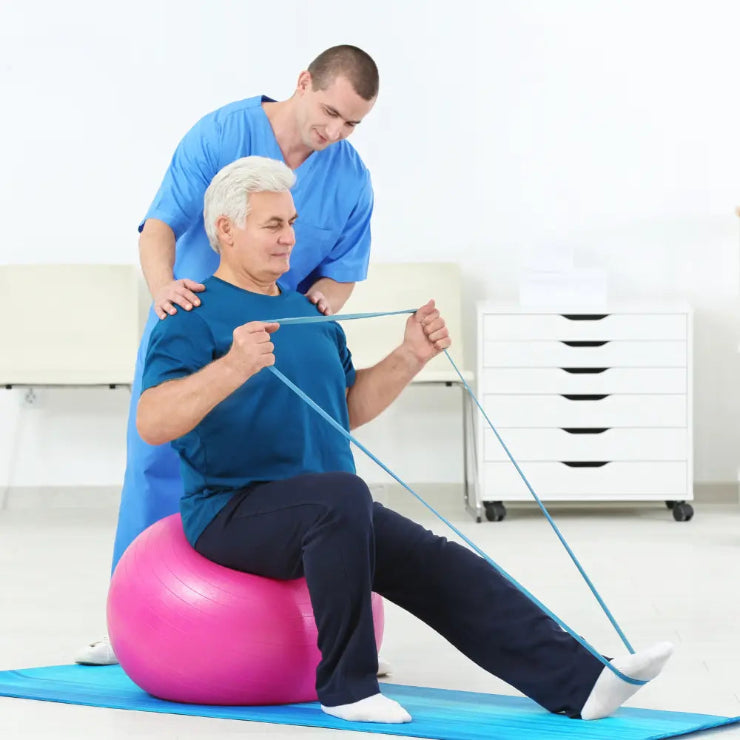 Physiotherapist assisting a patient on an exercise ball with resistance bands in a clinical setting.